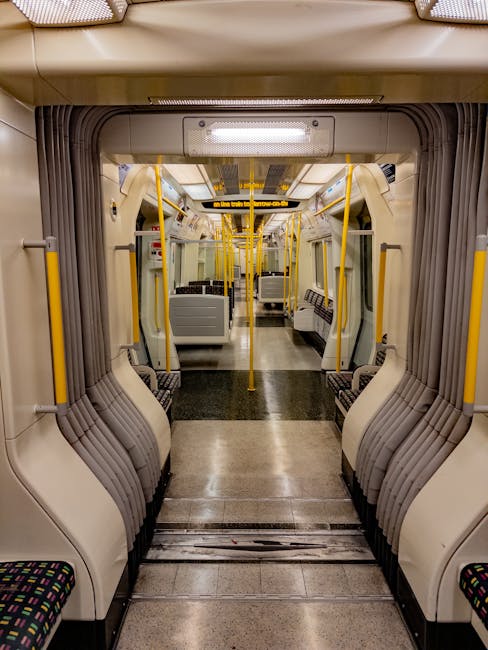 Interior view of a clean, modern train carriage with beige and grey plastic seating, patterned fabric upholstery on the seats, and yellow handrails and stanchions. The floor is smooth, polished, and free of dust or debris. Bright overhead lighting illuminates the space evenly, highlighting the shiny, well-maintained surfaces. The carriage appears hygienic and ready for passengers, with no visible dirt or clutter, reflecting professional cleaning and maintenance typical of services provided by Kennington Carpet Cleaners in the context of surface sanitisation and domestic cleaning for public transport environments.